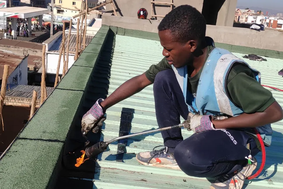 Artisan soudant une membrane sur un acrotère au bord d’une toiture en tôle.