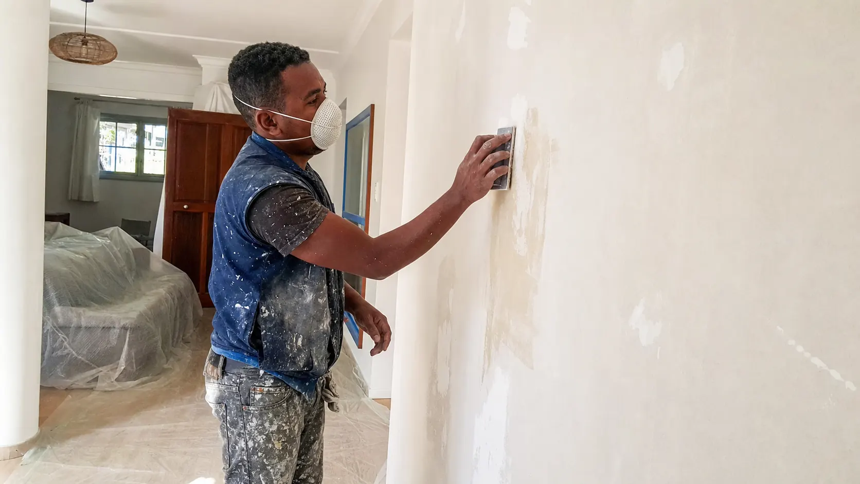Peintre préparant soigneusement un mur intérieur avant application de la peinture.
