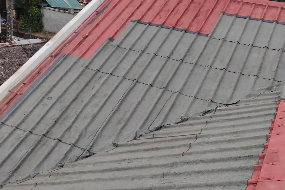 Toiture en tôle rouge en cours de recouvrement par une membrane d’étanchéité grise.